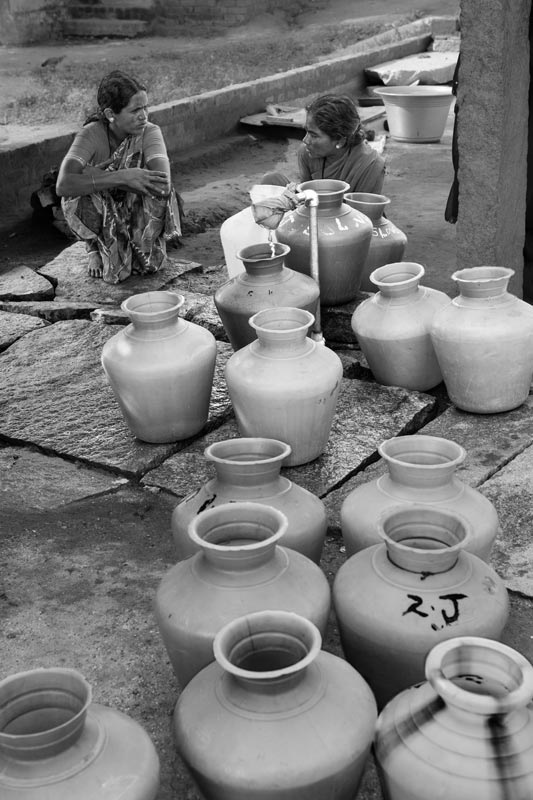 Waiting for the water trickle to fill the pitcher in a rural habitation in district Kolar, Karnataka